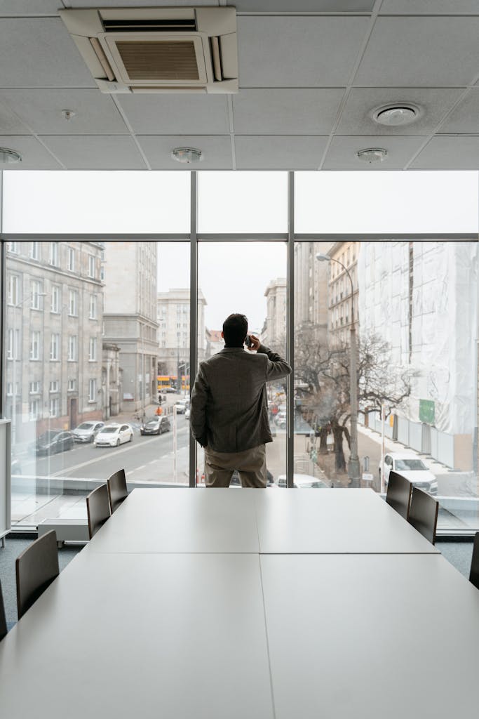 Businessman standing in a modern office, talking on the phone while looking out the window onto a city street.